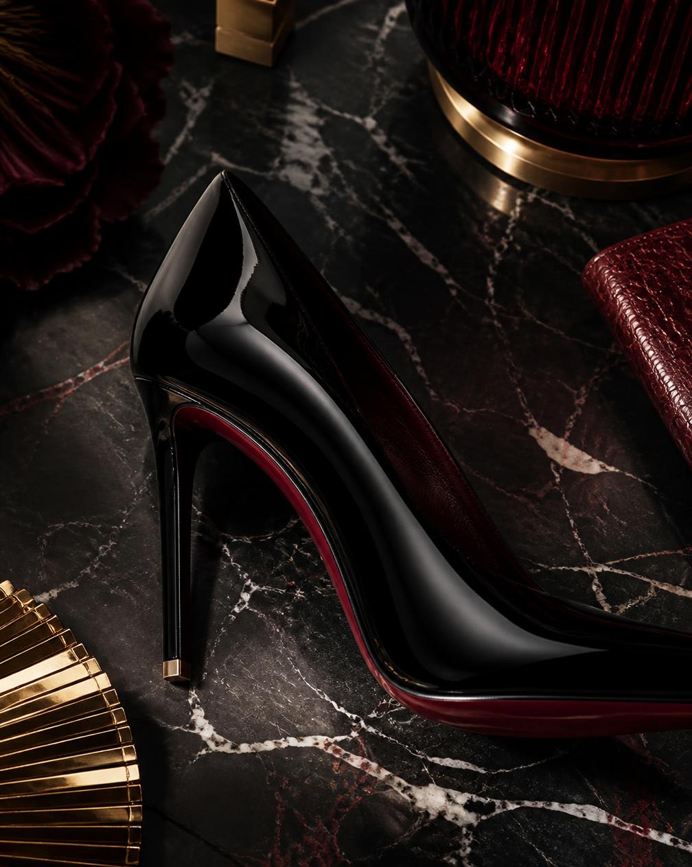 Black patent stiletto pump on dark veined marble in low side light